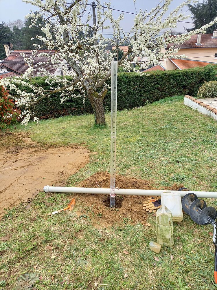 Un tuyau de puits d'eau en plastique transparent dans une cour avec un arbre en fleurs en arrière-plan.