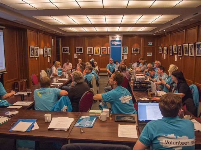 Eine Gruppe von Menschen sitzt an langen Tischen in einem Konferenzraum.
