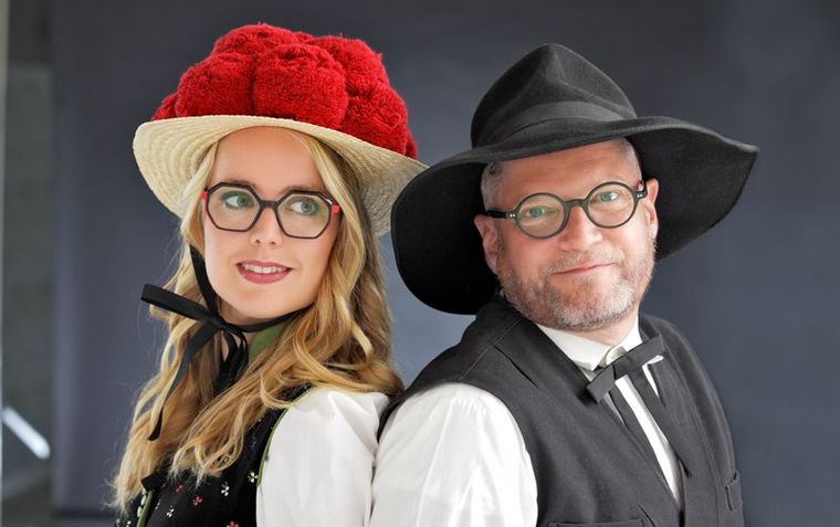 Ein Mann und eine Frau stehen Rücken an Rücken und tragen Hüte und Brillen.