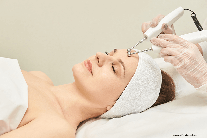 Frau erhält Gesichtsbehandlung mit Handgeräten; Spa-Atmosphäre.