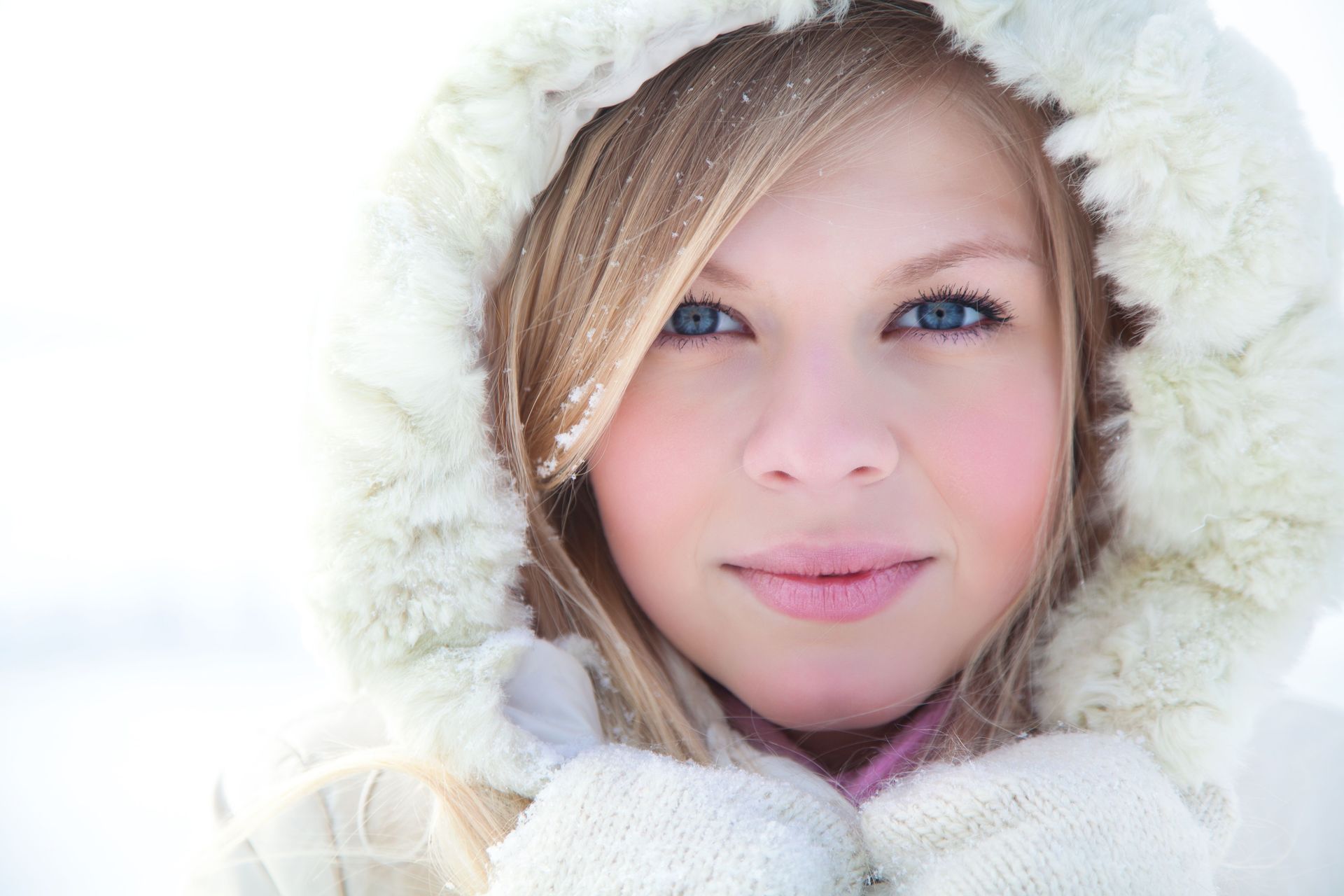 Una niña con una capucha de piel y guantes en la nieve.