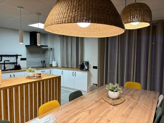 Una cocina con mesa y sillas y lámparas de mimbre colgando del techo.