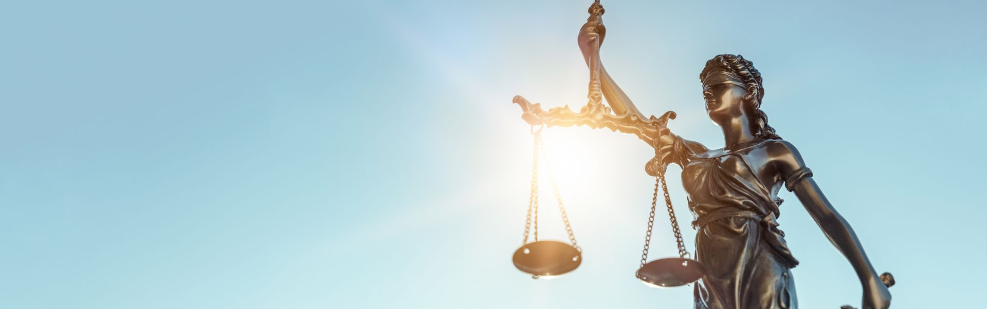 Statue de la justice avec balance, bras levé, se dressant sous un ciel lumineux.