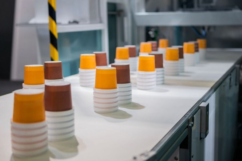 Una cinta transportadora llena de pilas de vasos de papel en una fábrica.