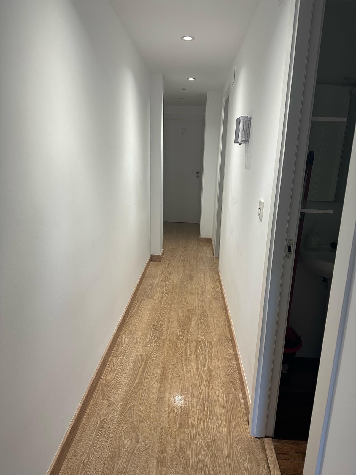 Un largo pasillo con suelo de baldosas y paredes blancas que conduce a un baño.