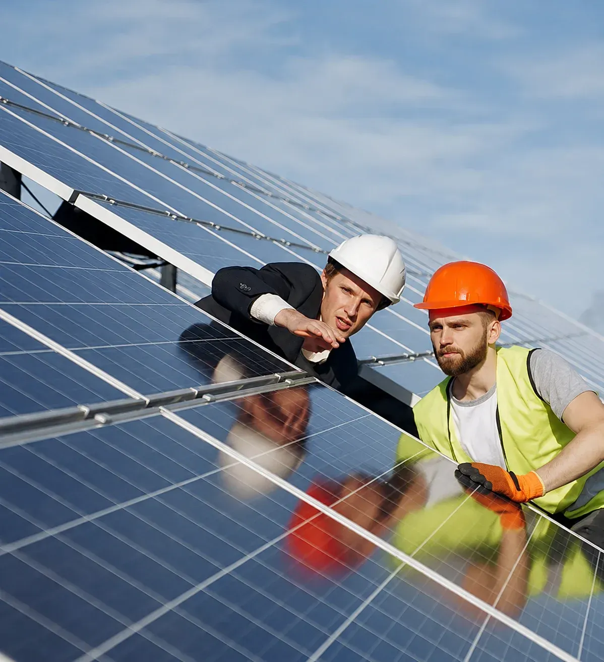Dos instaladores de paneles solares con cascos trabajando en un tejado bajo un cielo azul.
