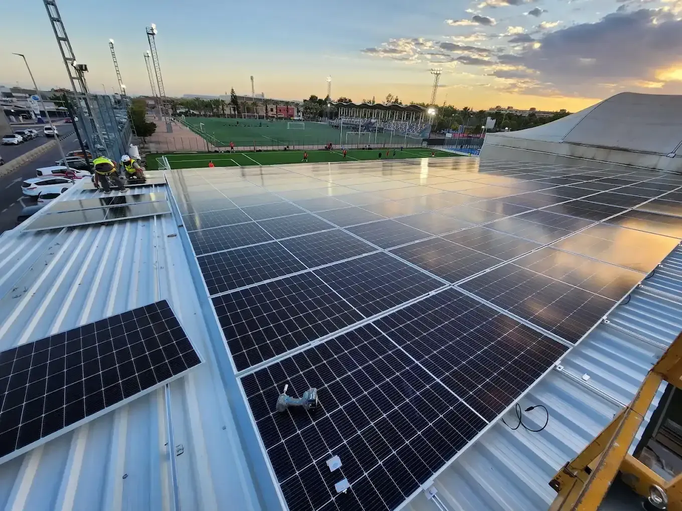 Paneles solares en una azotea al atardecer, con vistas a un campo deportivo.