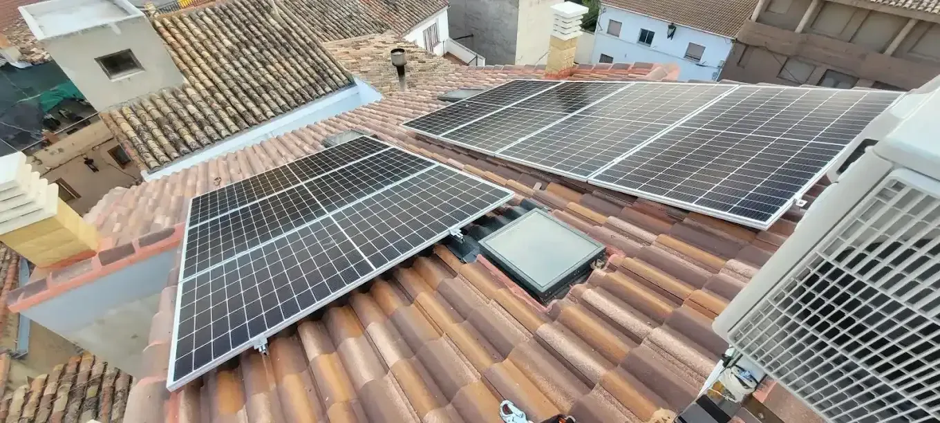 Paneles solares instalados en un tejado de tejas de terracota en un barrio residencial, vistos desde arriba.