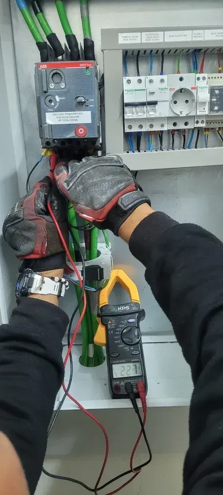 Electricista con guantes prueba un panel de interruptores con un multímetro en un armario eléctrico.