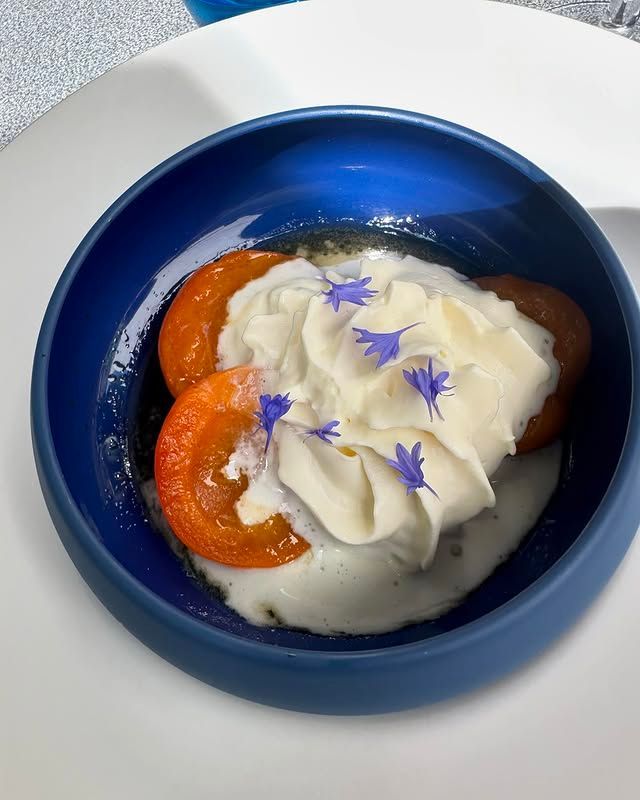 Bol bleu contenant un dessert garni de crème fouettée, de tranches d'orange et de pétales de fleurs violettes.