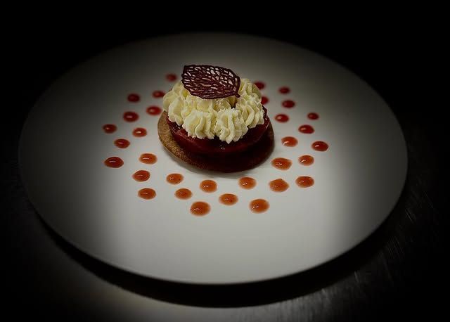 Dessert servi sur une assiette blanche, agrémenté de points de sauce rouge et d'une garniture en chocolat.