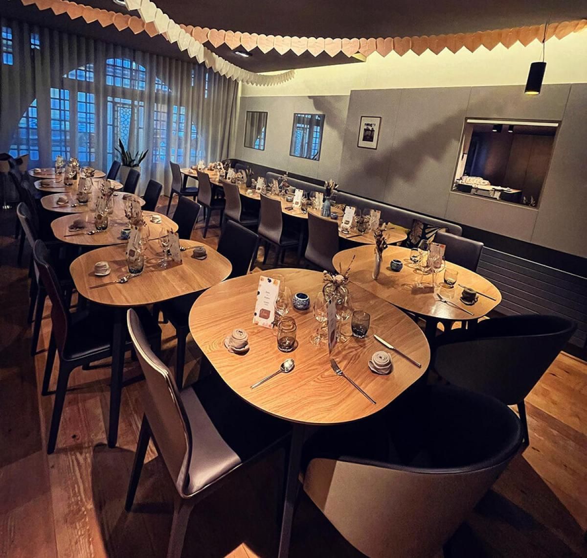 Salle à manger élégante d'un restaurant avec tables rondes en bois, chaises noires et grandes fenêtres