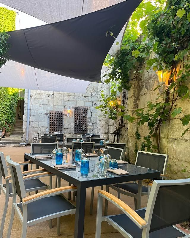 Terrasse extérieure avec table dressée sous une voile d'ombrage noire et verdure sur les murs en pierre