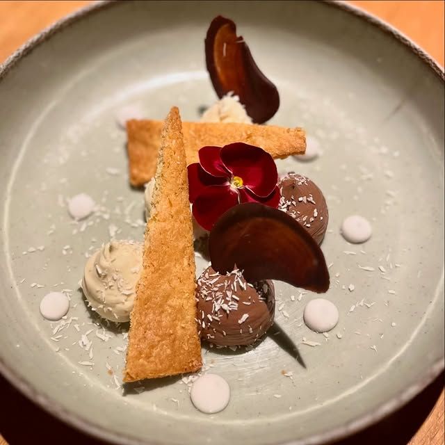 Assiette de dessert composée de mousse au chocolat, de gaufrettes croustillantes, d'une garniture de fleurs rouges et de quenelles blanches.