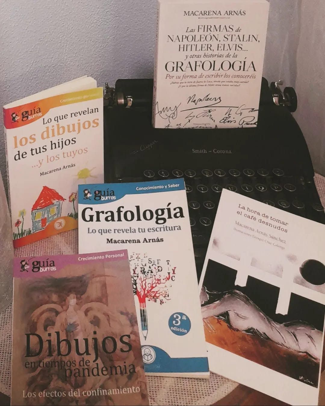Libros y una máquina de escribir negra dispuestos sobre una mesa, con portadas y papeles españoles cerca.