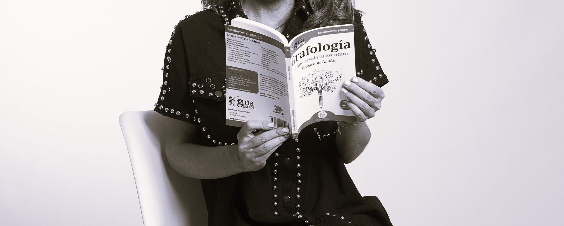 Una mujer está sentada en una silla leyendo un libro.