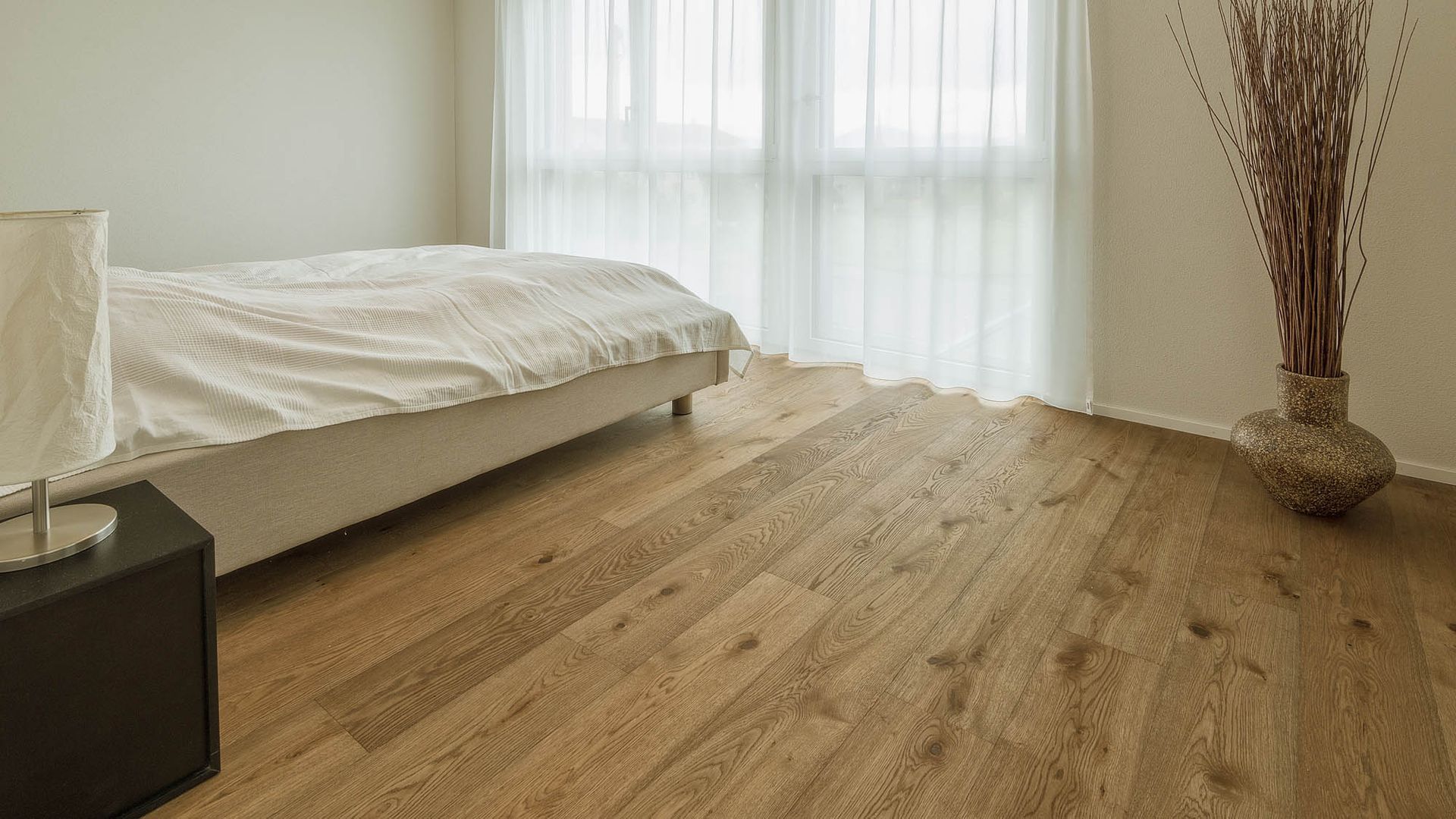 Ein Schlafzimmer mit Hartholzböden, einem Bett, einer Lampe und einer Vase mit Blumen.