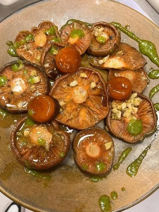 Champiñones y tomates salteados rociados con salsa verde en un plato beige.