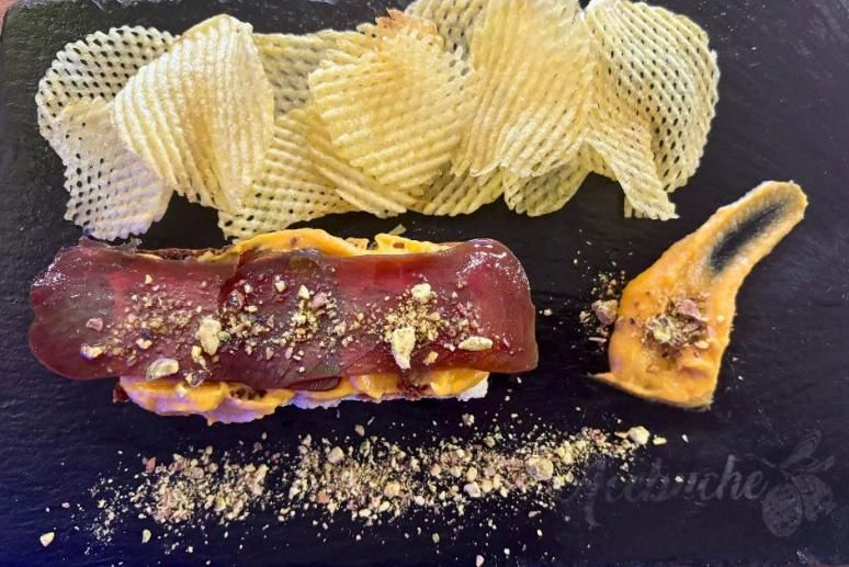 Aperitivo: Carne cortada en rodajas sobre una base, con patatas fritas y salsa, sobre una pizarra negra.