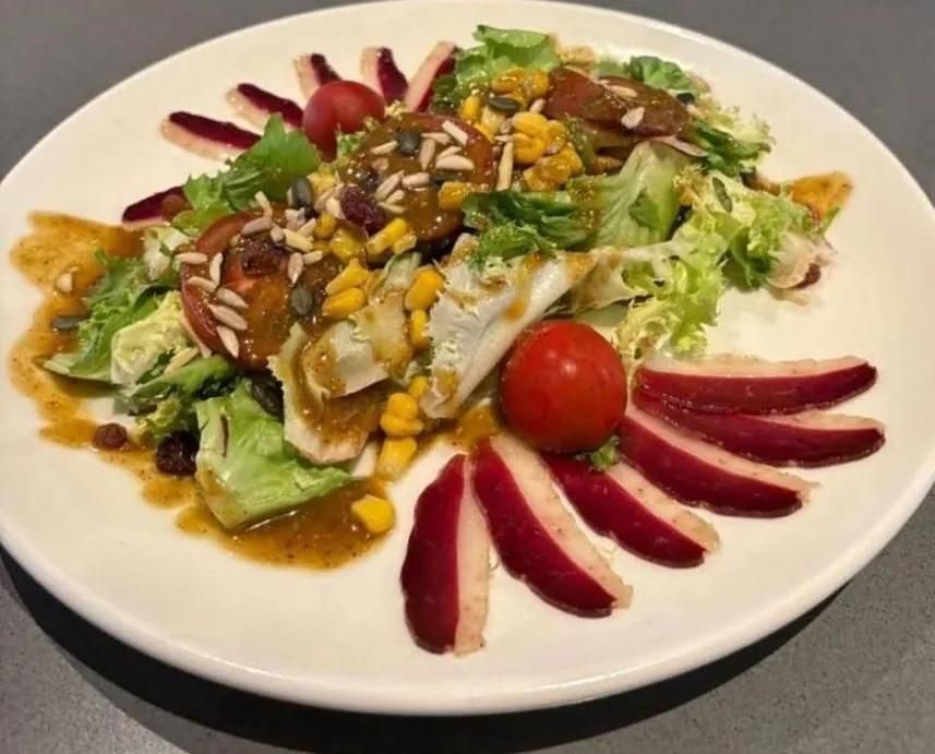 Ensalada con tomates, maíz, semillas de girasol y rodajas de manzana roja, en un plato blanco.