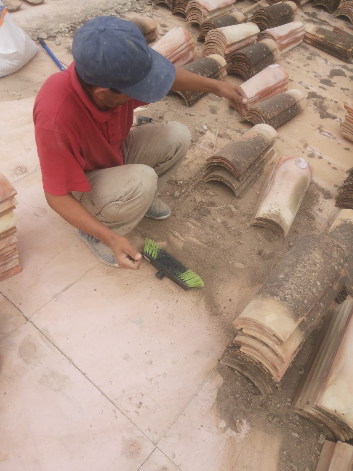 Un hombre con una camisa roja y un sombrero azul está limpiando una pila de ladrillos.