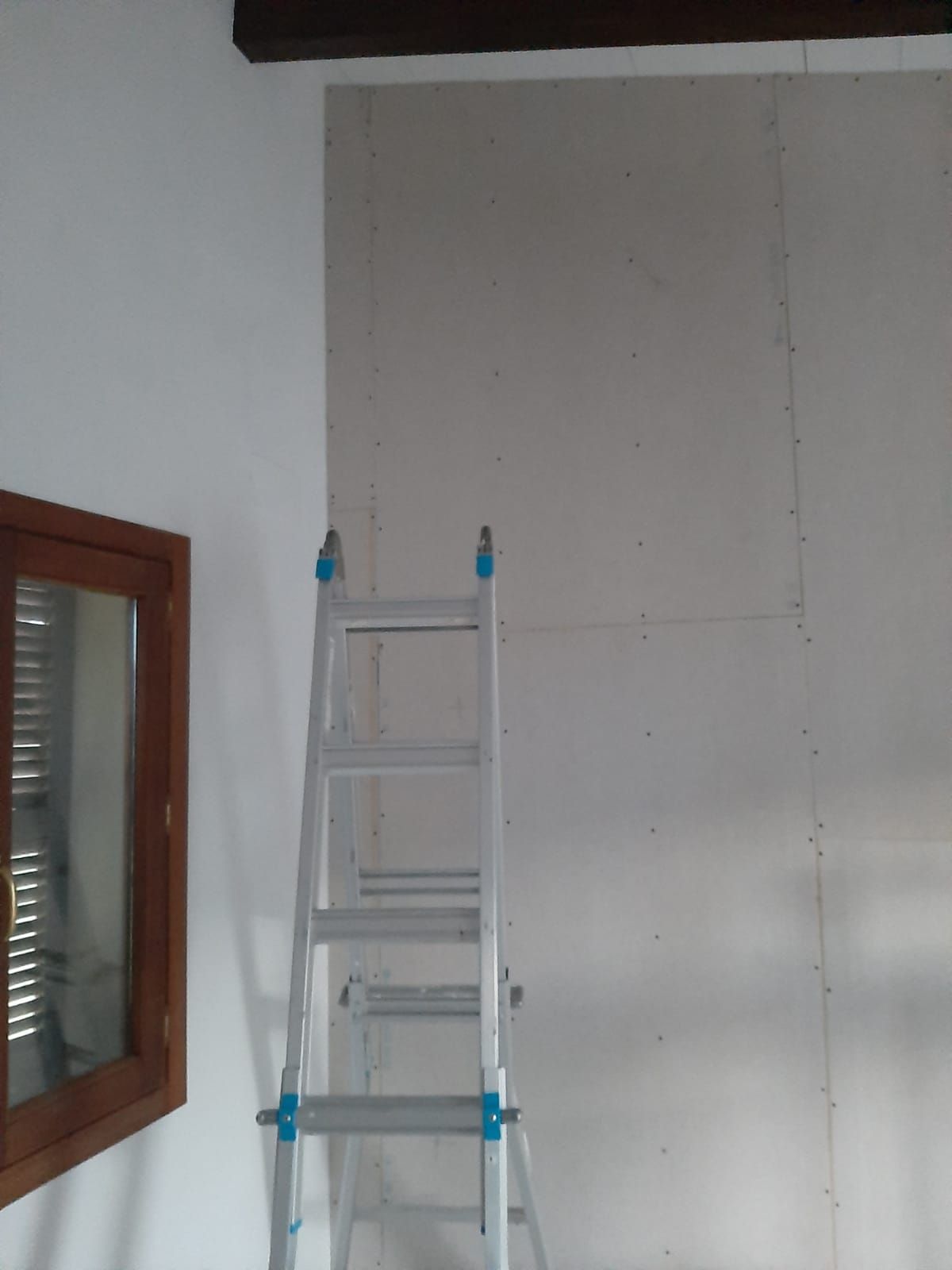Una escalera está apoyada contra una pared al lado de una ventana.