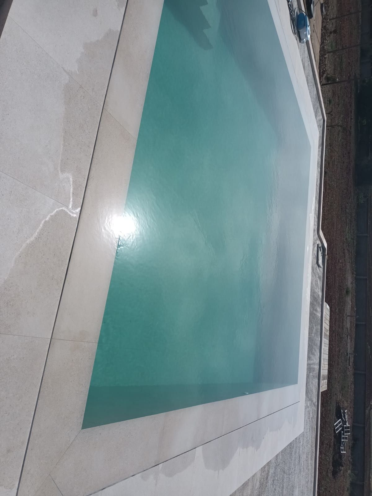 Una gran piscina con borde blanco y un reflejo del sol en el agua.