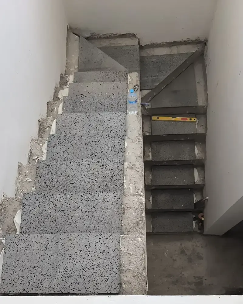 Escalera de hormigón con un separador central y una cinta métrica amarilla en los escalones de la derecha.