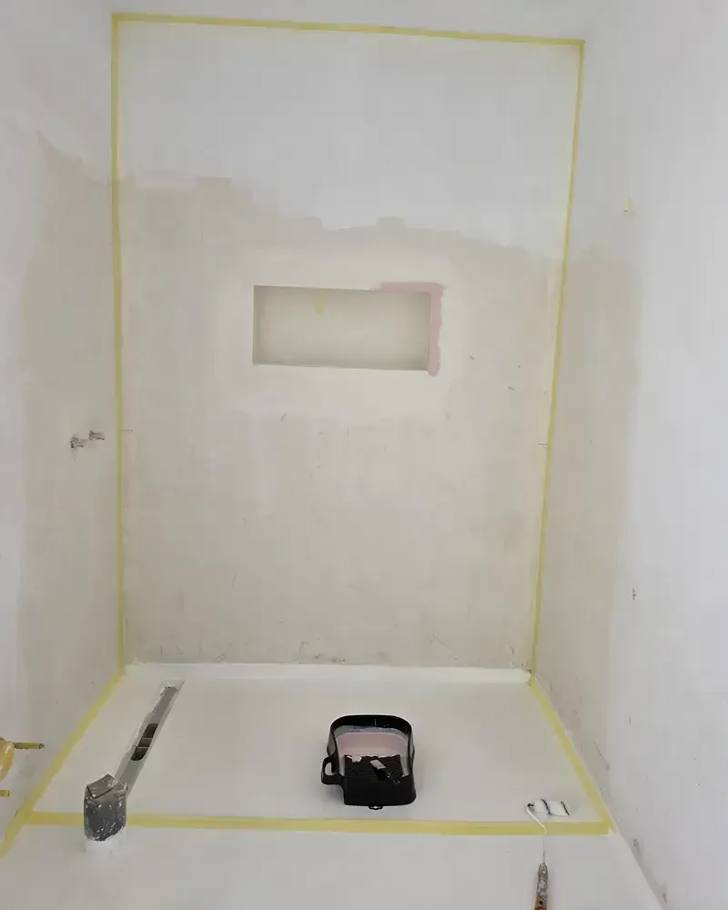 Habitación pequeña sin terminar, con bordes sellados con cinta adhesiva, un nicho en la pared y herramientas en el suelo.