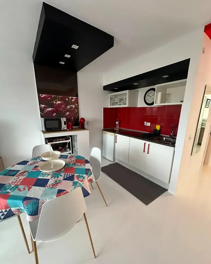 Cocina y comedor modernos con gabinetes rojos, mesa blanca y detalles en el techo negro.