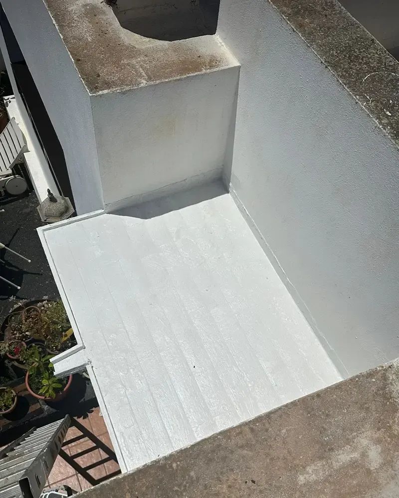 Terraza blanca vacía en la azotea, rodeada de muros y con una cornisa marrón bañada por la luz del sol.