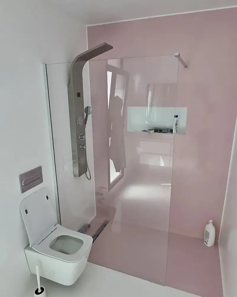 Baño moderno con paredes rosas, ducha de cristal, inodoro suspendido y nicho para el lavabo.