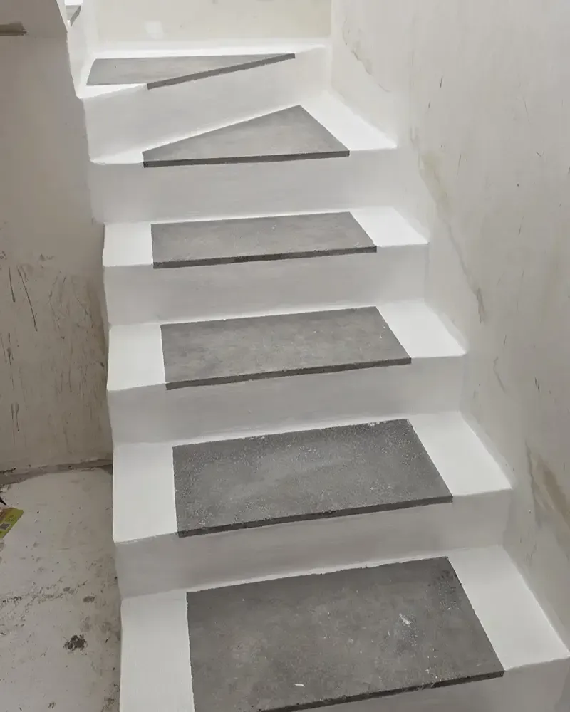 Escalera de hormigón blanco con peldaños grises y paredes laterales blancas dentro de una habitación sin terminar.