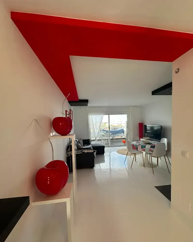 Salón moderno de planta abierta con un llamativo techo rojo, suelos blancos y mesa de comedor cerca de grandes ventanales.