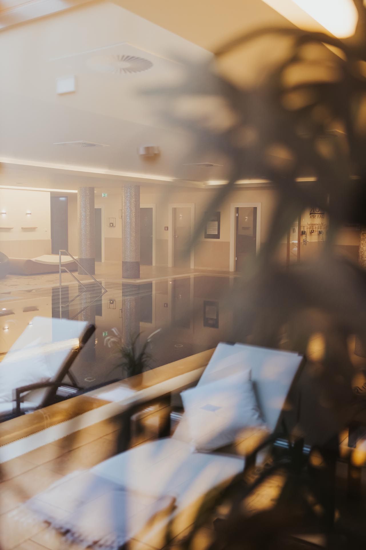 Gemütlicher Sitzbereich in der Lobby mit beigefarbenen Liegestühlen und verschwommenen Pflanzenblättern im Vordergrund