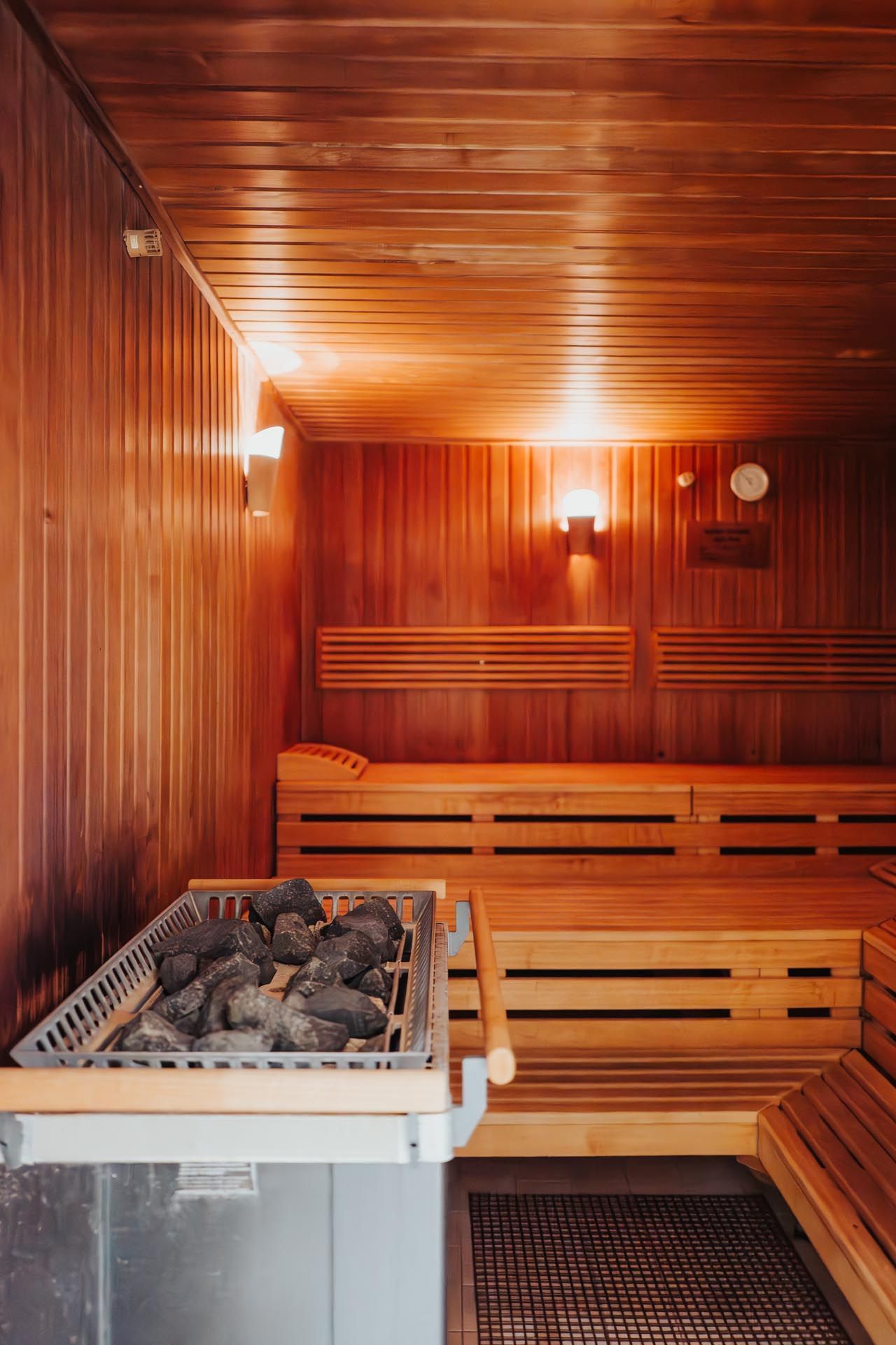 Holzgetäfelte Sauna mit Holzbänken und einem mit Steinen gefüllten Ofen.