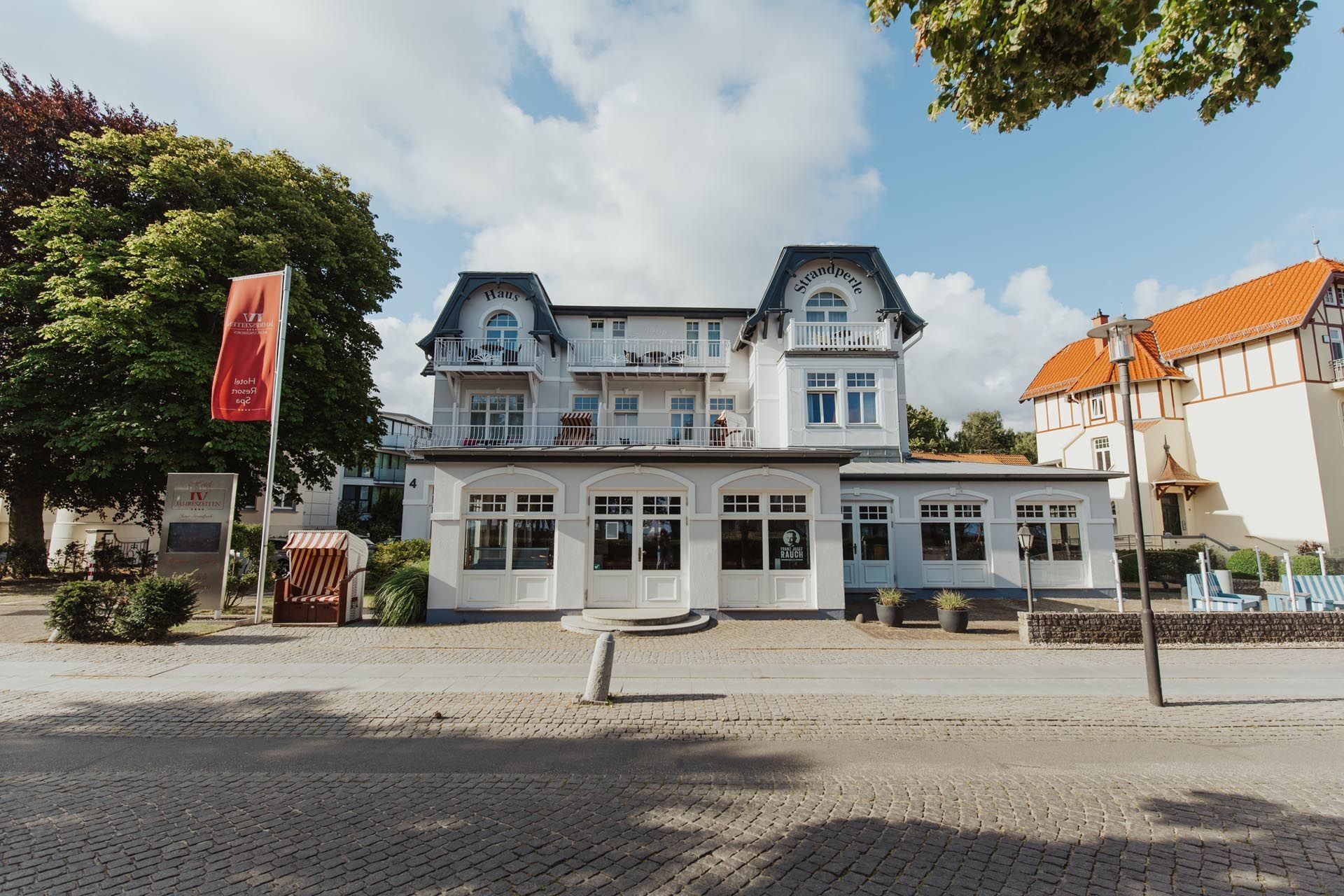 Weißes historisches Gebäude mit blau umrandeten Dachgauben in einer Kopfsteinpflasterstraße unter sonnigem Himmel