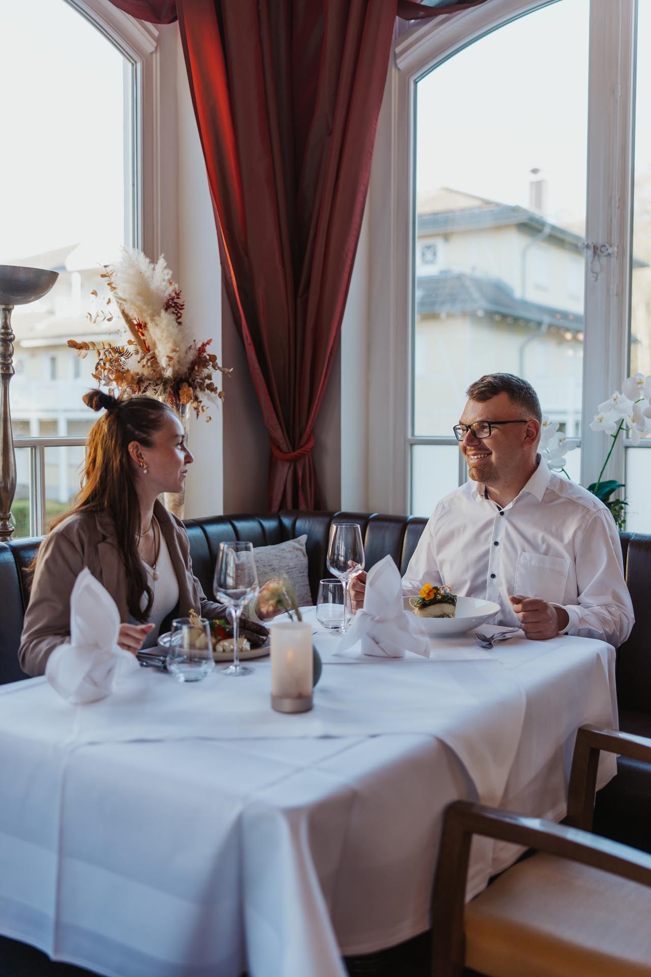 Zwei Personen speisen an einem Tisch am Fenster in einem schwach beleuchteten Restaurant.