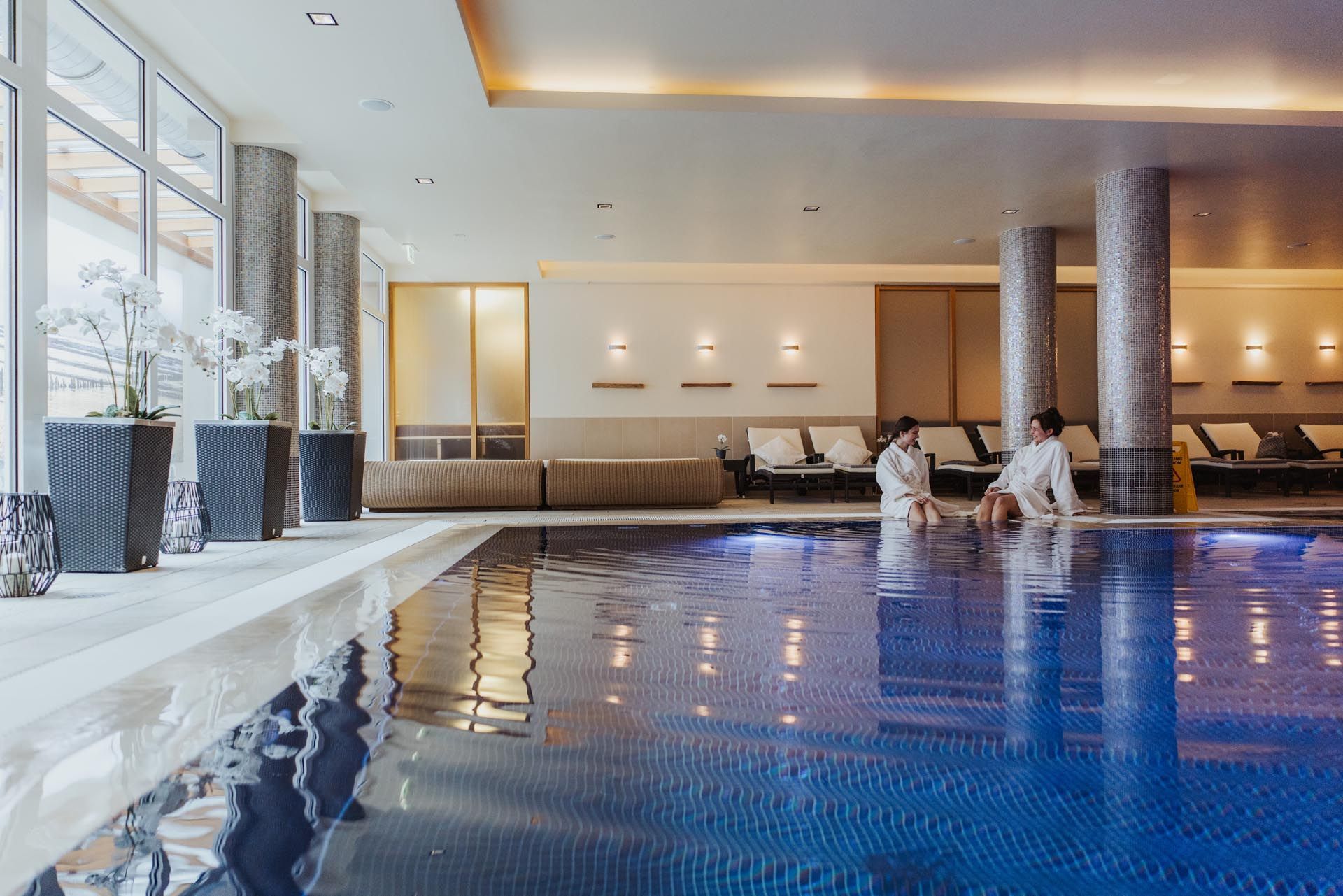Hotel-Innenpool mit blauem Wasser, Liegestühlen und Menschen, die sich am Beckenrand entspannen