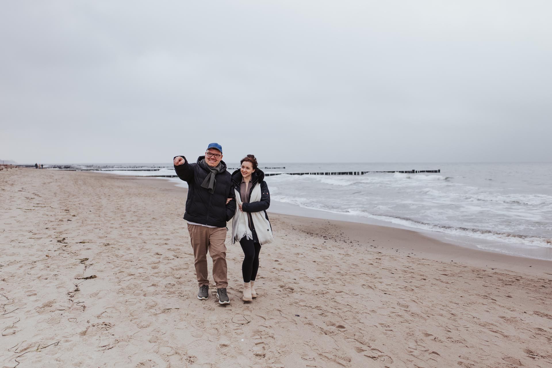 Zwei Personen spazieren unter grauem Himmel an einem Sandstrand entlang.