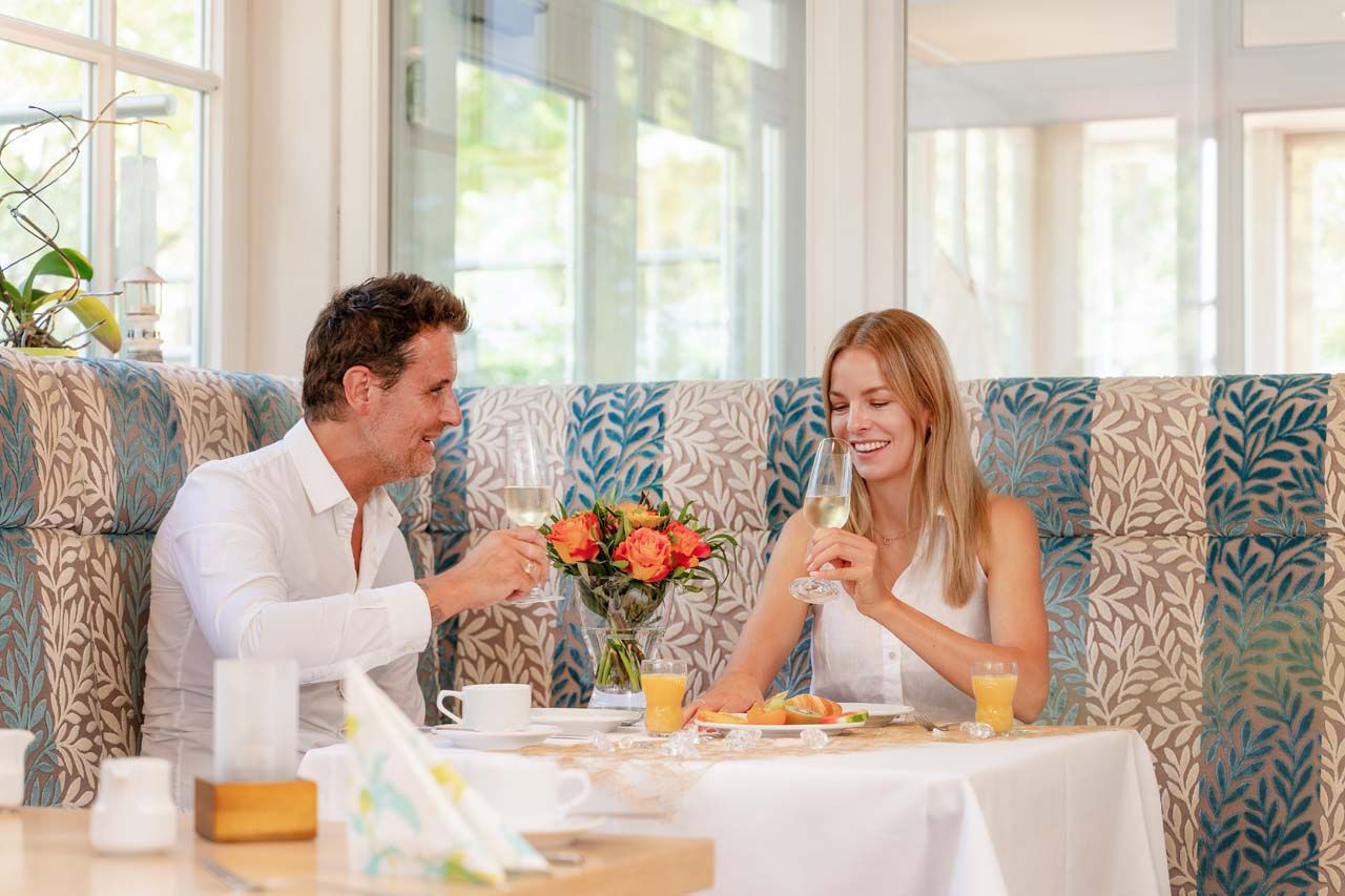 Ein Mann und eine Frau sitzen in einem Restaurant an einem Tisch und stoßen mit Sektgläsern an.