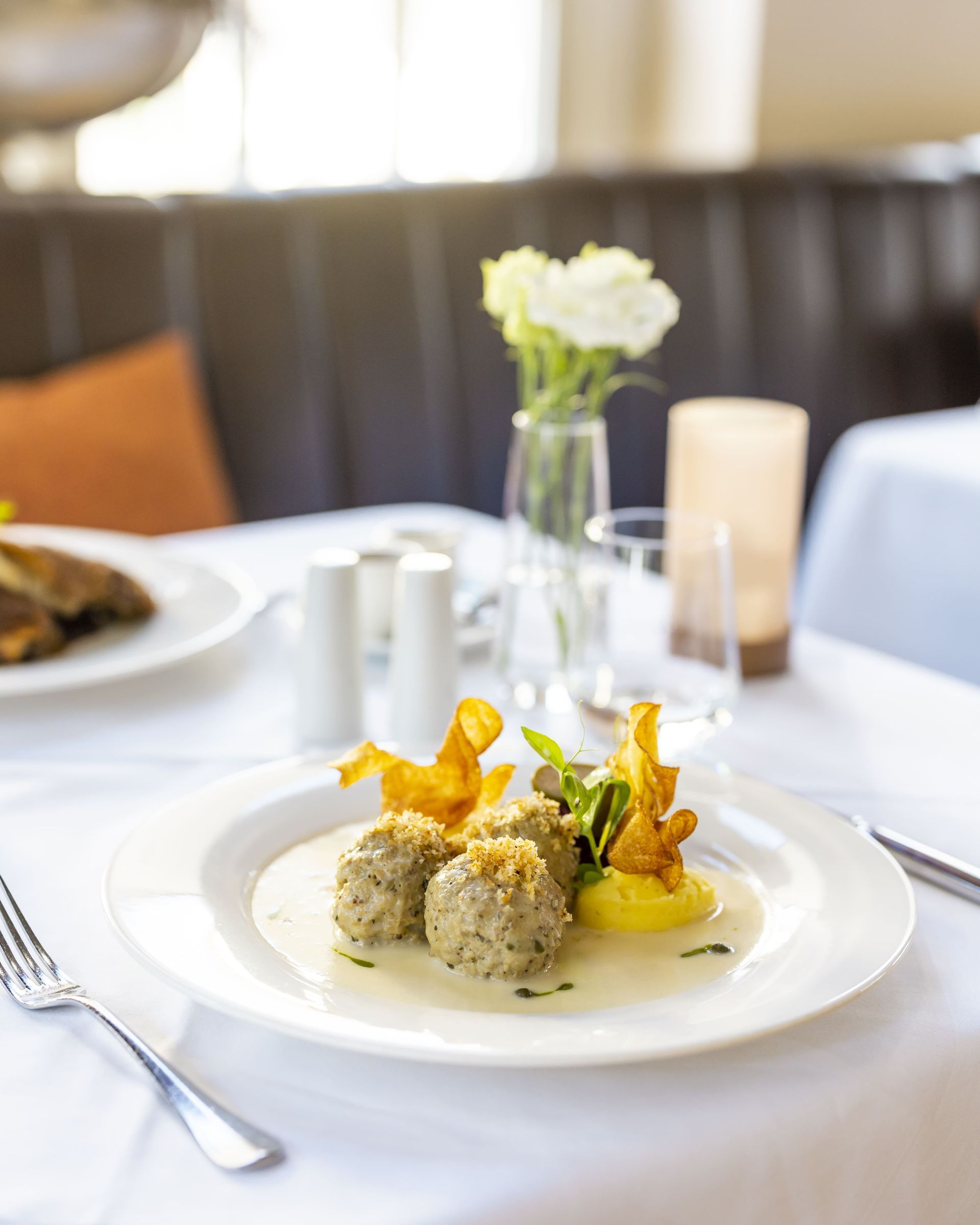 Ein Teller auf einem schön gedeckten Tisch mit Fleischbällchen und Gemüse, edel dekoriert.