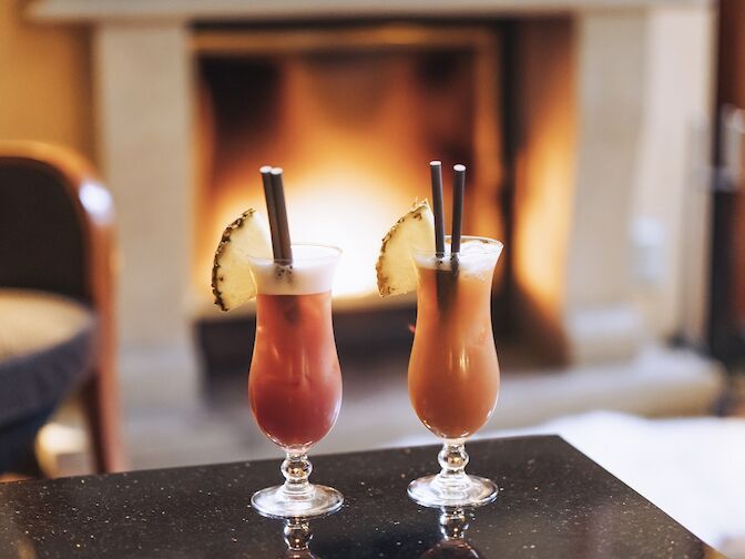 Zwei Cocktails stehen auf einem Tisch vor einem Kamin.