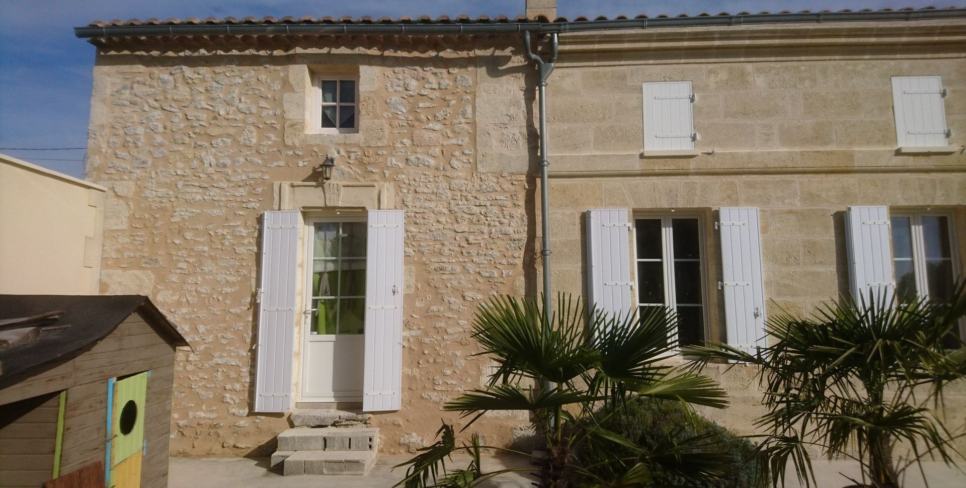 Une façade en pierre avec des portes et fenêtres aux volets blancs