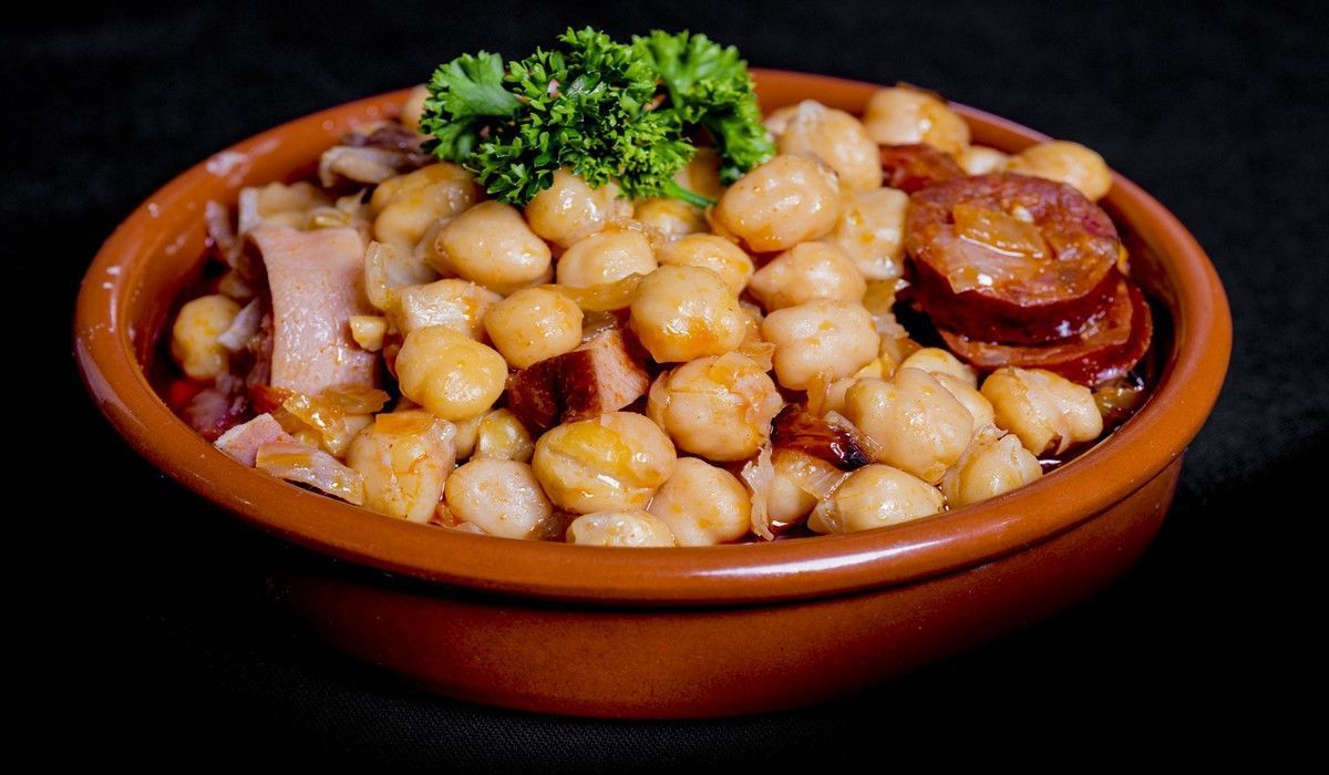 Un bol de garbanzos con chorizo ​​y perejil encima.