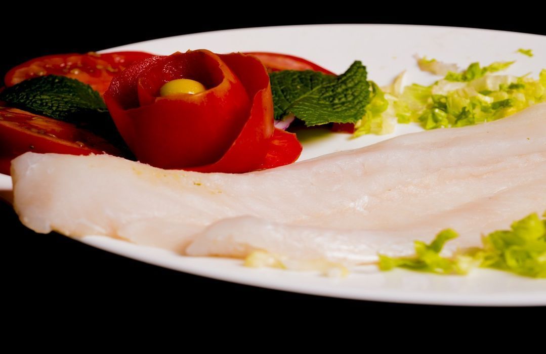 Un plato blanco cubierto con pescado y verduras sobre un fondo negro.