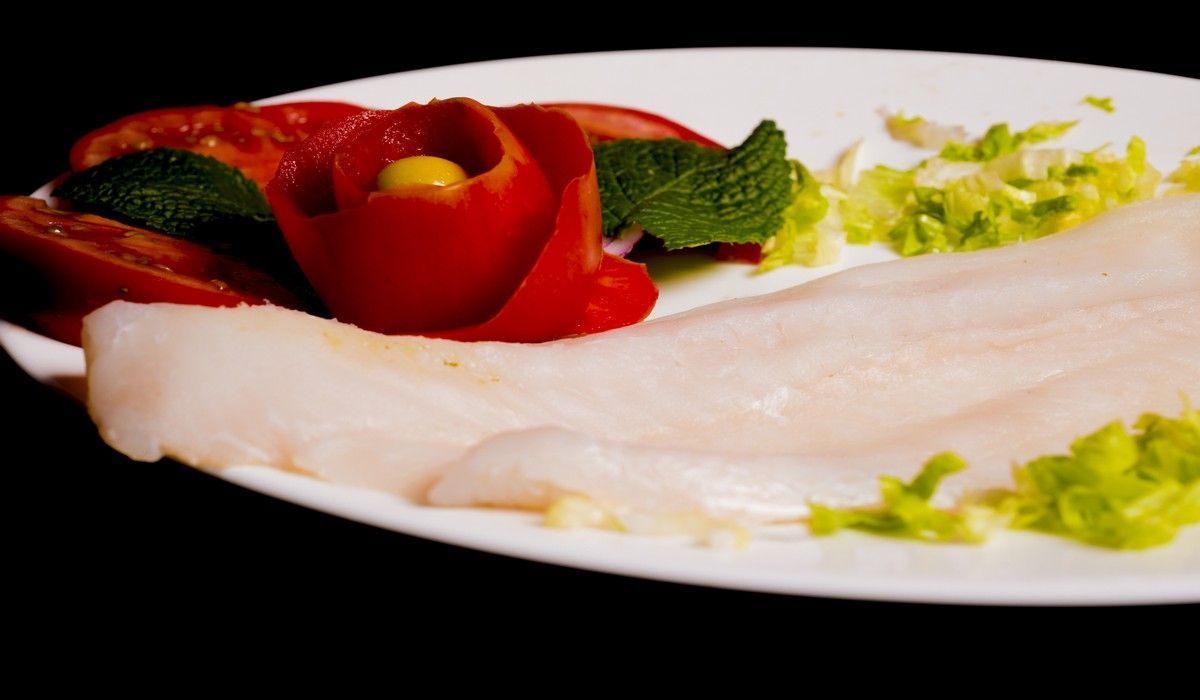 Un plato blanco cubierto con pescado y verduras sobre un fondo negro.