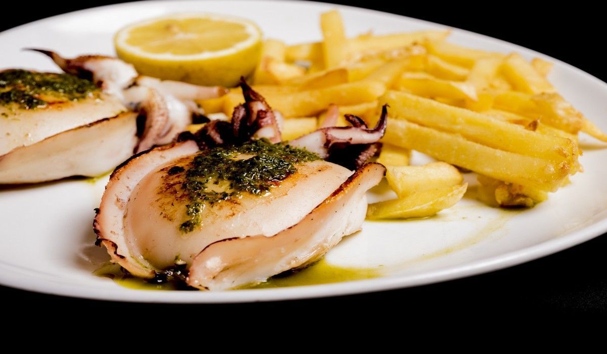 Un plato de comida con patatas fritas y calamares encima.