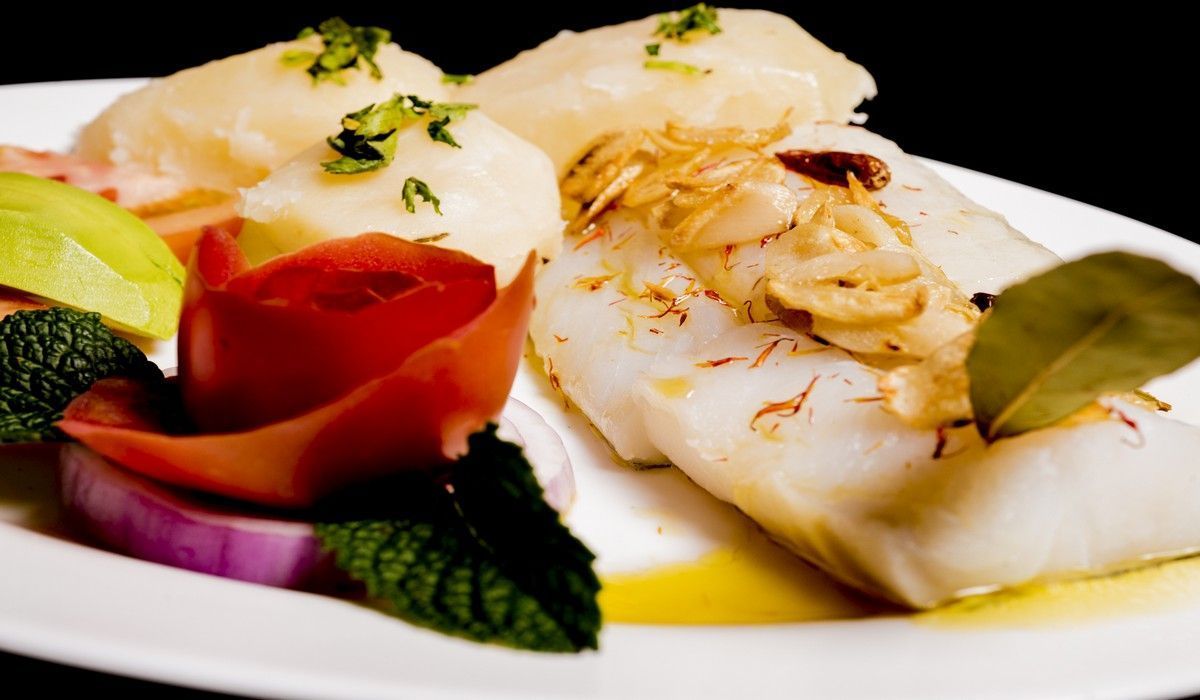 Un plato blanco cubierto con pescado y verduras sobre un fondo negro.