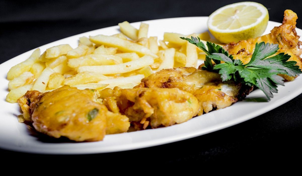 Un plato blanco cubierto con pescado frito y papas fritas.